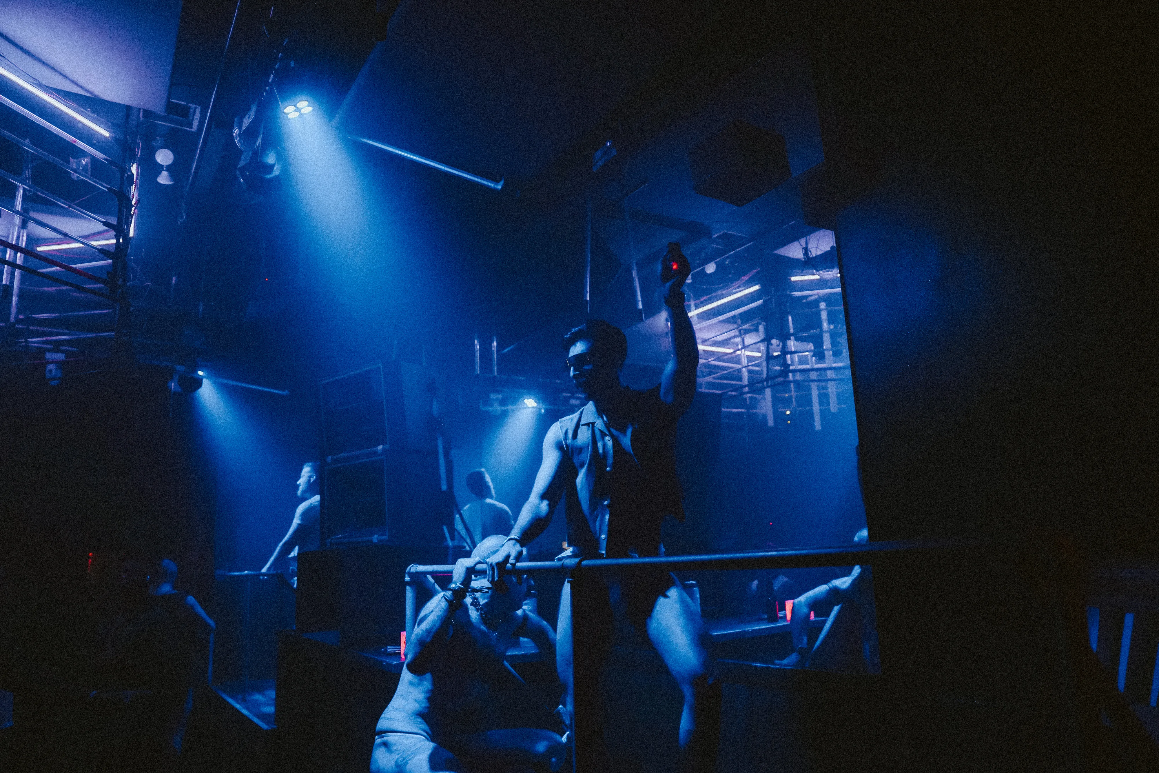 Partygoer in sunglasses raises a drink at the railing under blue stage lights